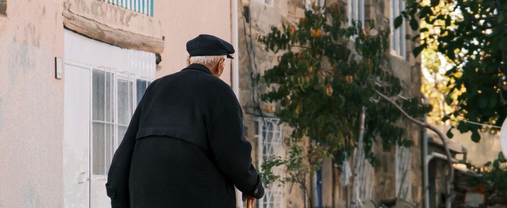 Anziano con il bastone che cammina in una strada di paese