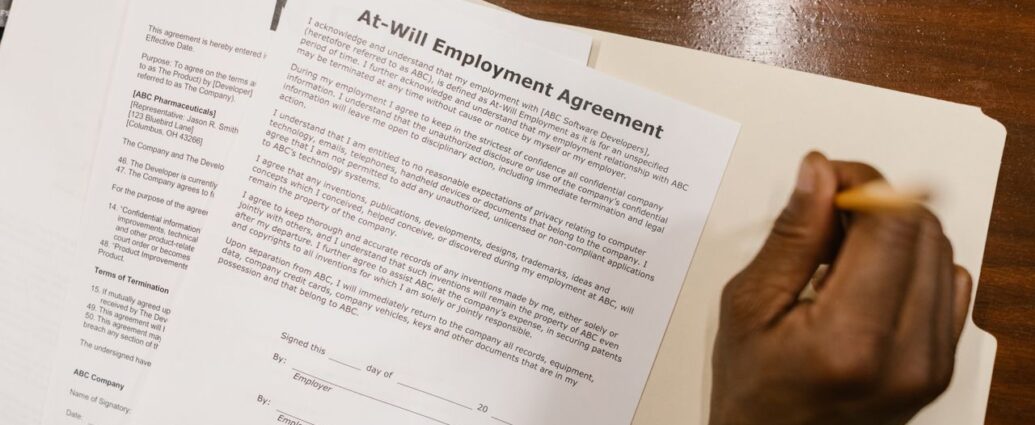 Mano che firma un contratto di lavoro su una scrivania in legno