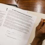 Mano che firma un contratto di lavoro su una scrivania in legno